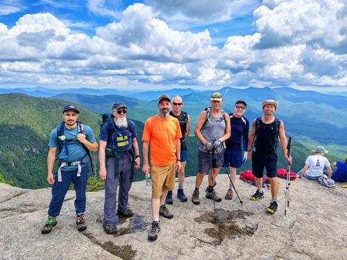 A group of GayOutdoors hikers on a mountain summit with mountain views behind them