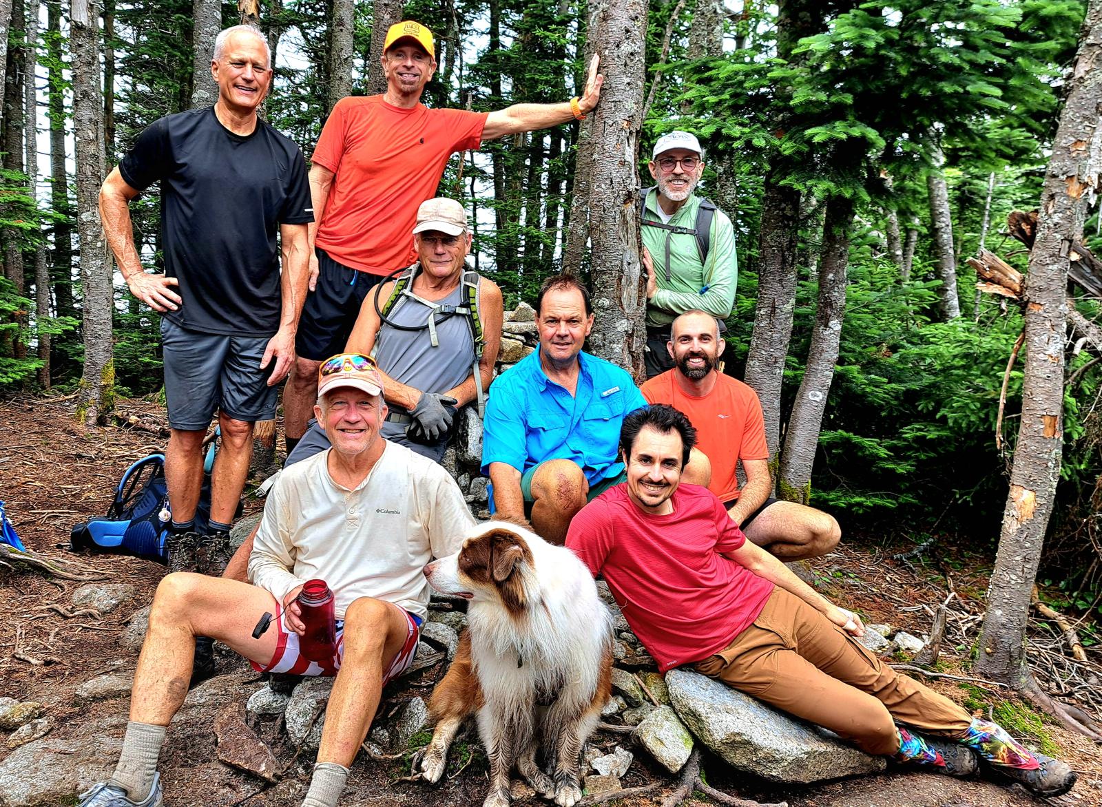 GayOutdoors volunteers and a dog resting together among spruce trees after a trail day