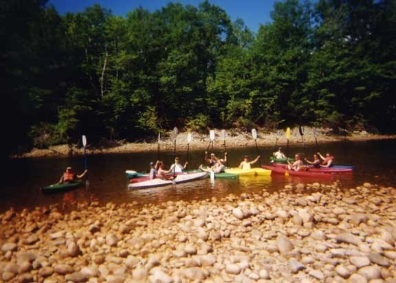 A group of GayOutdoors members paddling kayaks together on a calm river