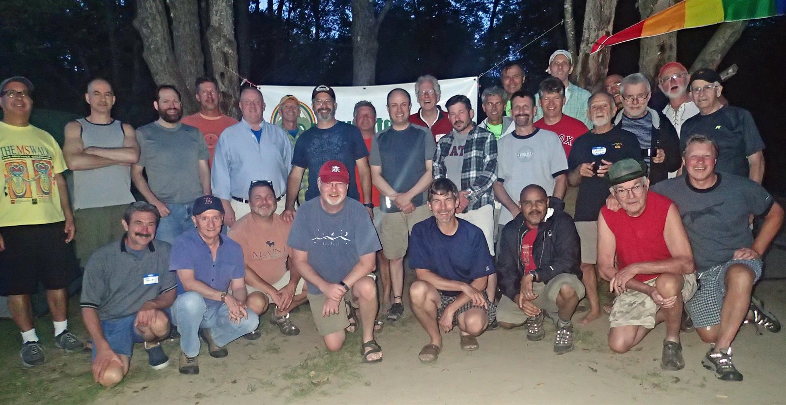 A large group of GayOutdoors members gathered together under a rainbow flag