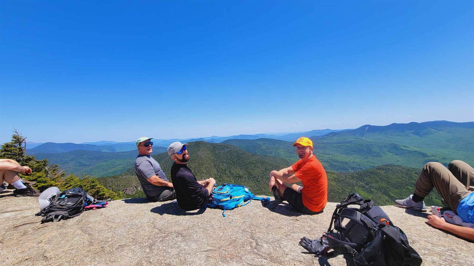 Three GayOutdoors members resting on a sunny summit ledge with mountain views
