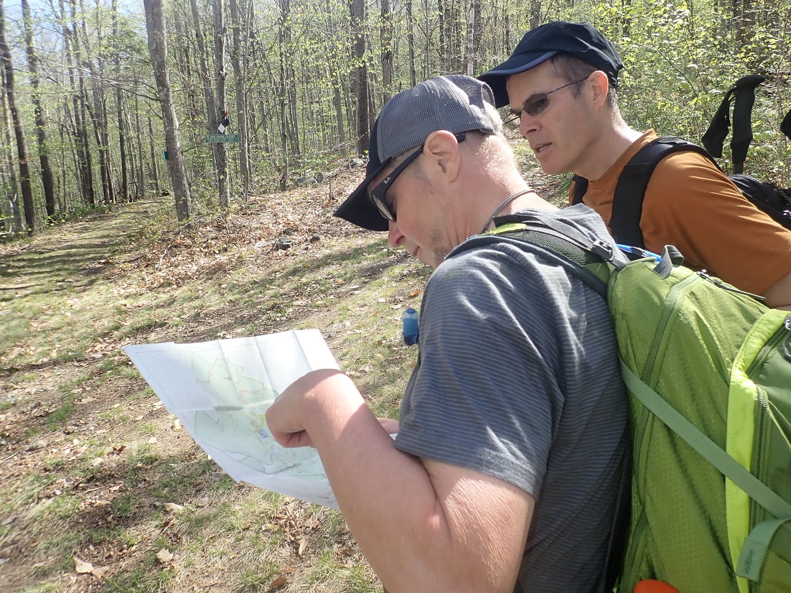 Two GayOutdoors hikers studying a paper trail map together at a trail junction