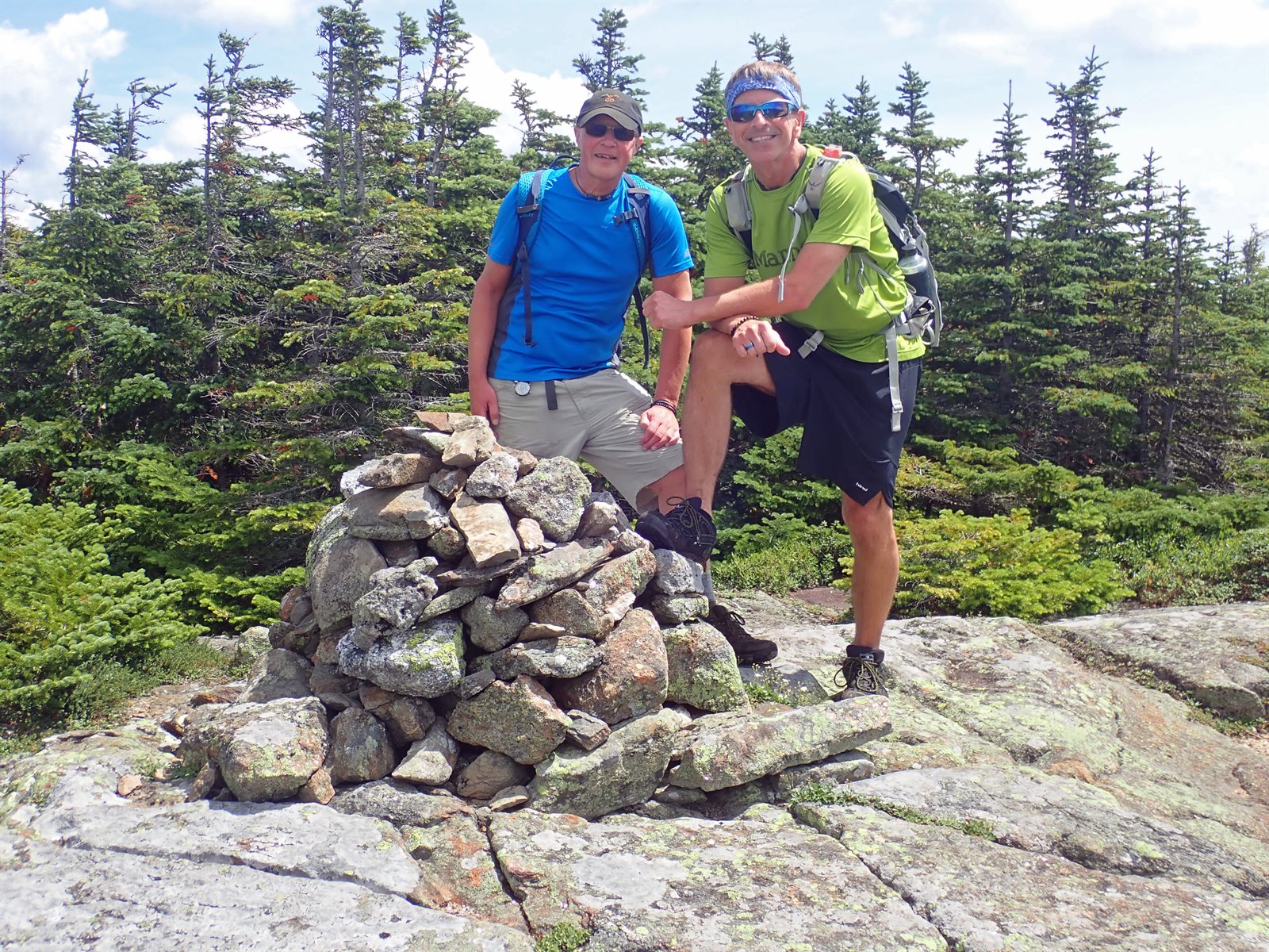 Two smiling GayOutdoors hikers with day packs beside a summit cairn