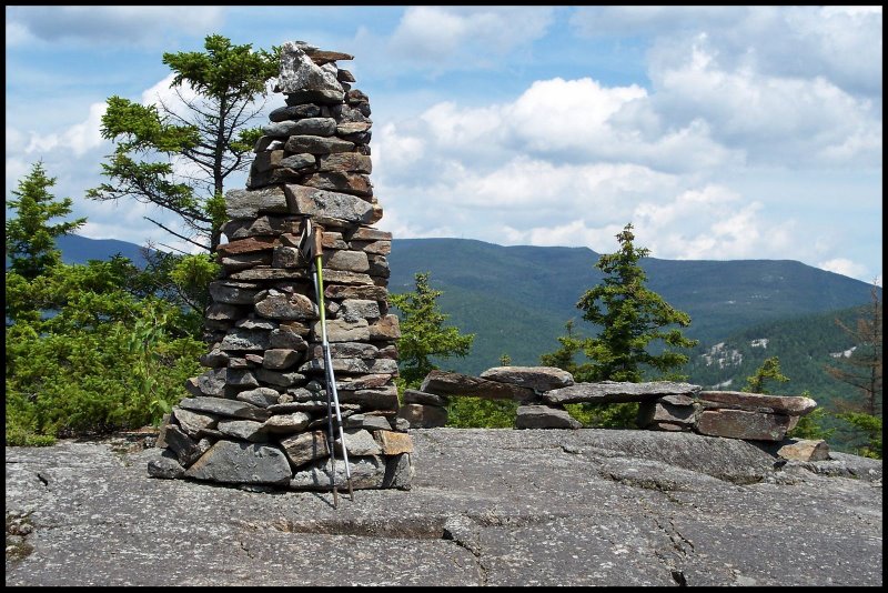 A summit cairn and trekking poles on an open ledge