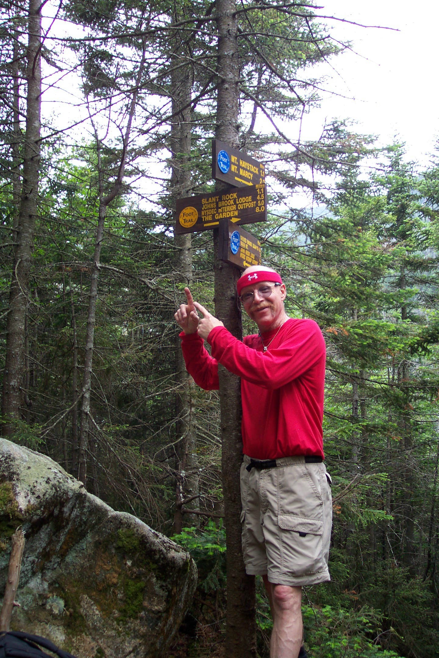 A smiling hiker pointing toward a trail sign